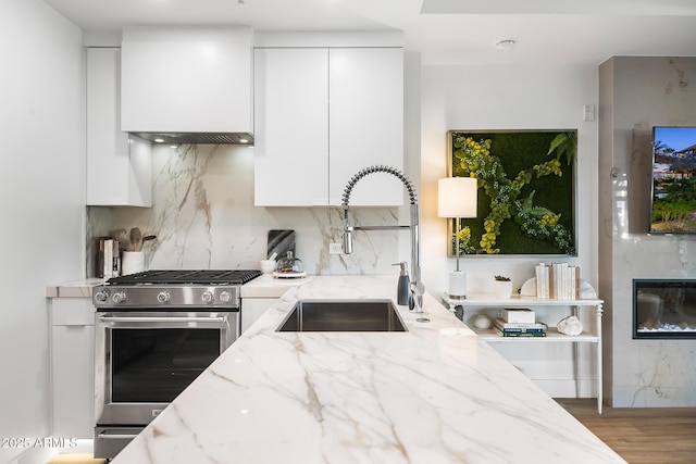 kitchen with sink, white cabinetry, tasteful backsplash, stainless steel range with gas cooktop, and light stone countertops