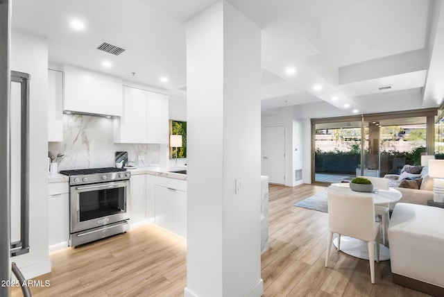 kitchen with tasteful backsplash, stainless steel range with gas cooktop, white cabinets, and light hardwood / wood-style flooring