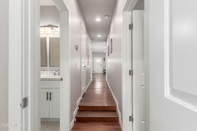 hallway featuring recessed lighting, wood finished floors, baseboards, and a sink