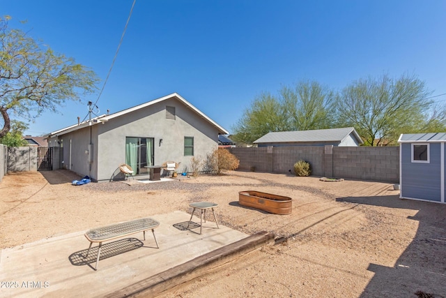 rear view of house featuring stucco siding, an outbuilding, a fenced backyard, an outdoor fire pit, and a storage shed