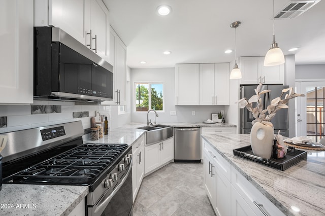 kitchen with light stone countertops, white cabinetry, sink, stainless steel appliances, and decorative light fixtures