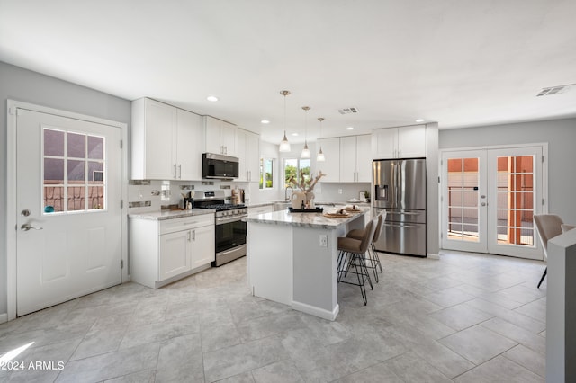 kitchen featuring french doors, light stone counters, stainless steel appliances, a center island, and hanging light fixtures