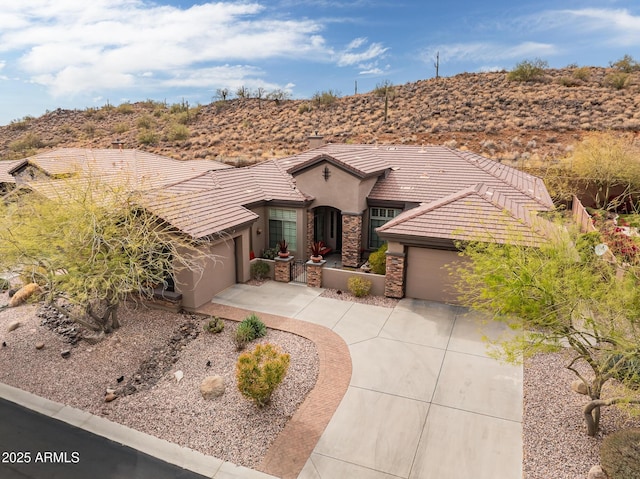 view of front of property featuring a tile roof, stucco siding, an attached garage, stone siding, and driveway