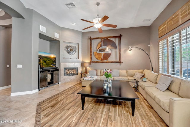 living room featuring light wood-type flooring, ceiling fan, and a tiled fireplace