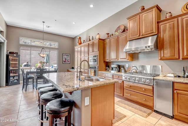 kitchen featuring appliances with stainless steel finishes, light stone counters, pendant lighting, a kitchen bar, and a kitchen island with sink