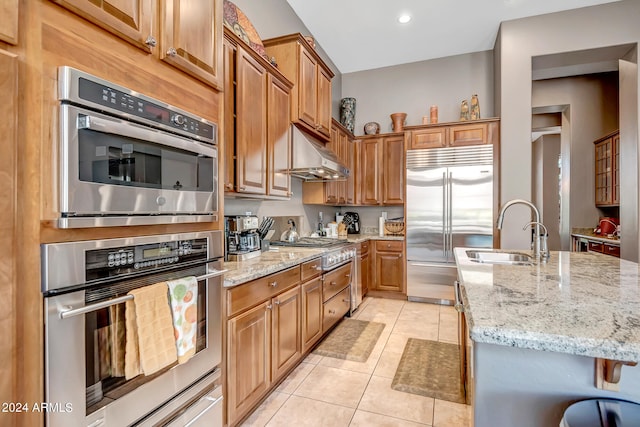 kitchen with light stone countertops, light tile patterned floors, stainless steel appliances, and sink