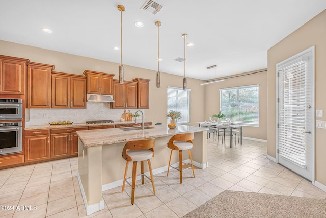 kitchen with visible vents, under cabinet range hood, a sink, backsplash, and brown cabinetry