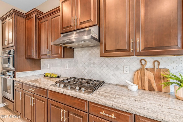 kitchen featuring under cabinet range hood, stainless steel appliances, light stone counters, and backsplash