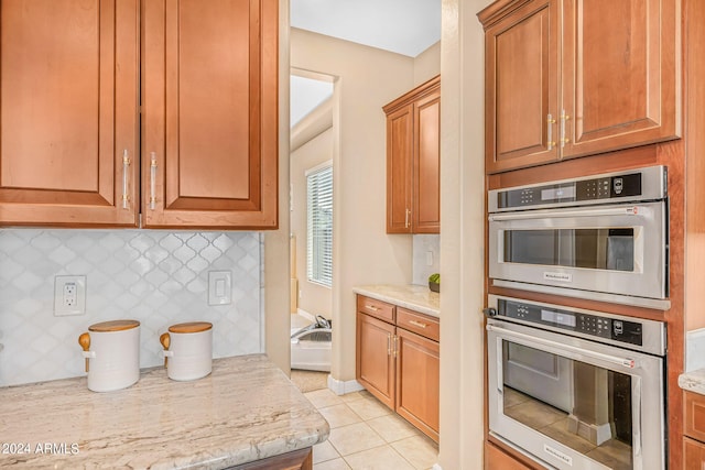 kitchen featuring tasteful backsplash, light tile patterned floors, double oven, and light stone countertops