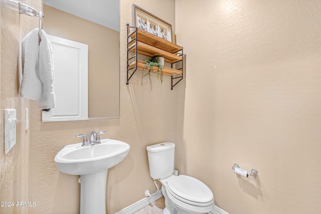 half bath featuring toilet, baseboards, and a sink