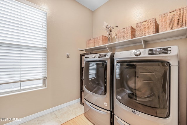 clothes washing area featuring light tile patterned flooring, laundry area, washer and dryer, and baseboards