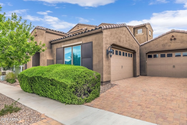 mediterranean / spanish home featuring stucco siding, an attached garage, a tile roof, and decorative driveway