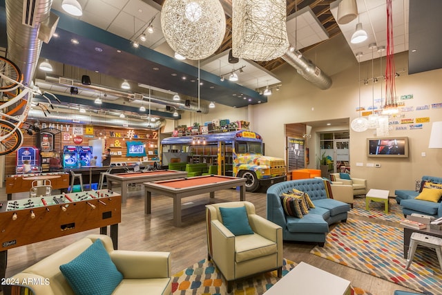 playroom with billiards, rail lighting, wood finished floors, and a towering ceiling