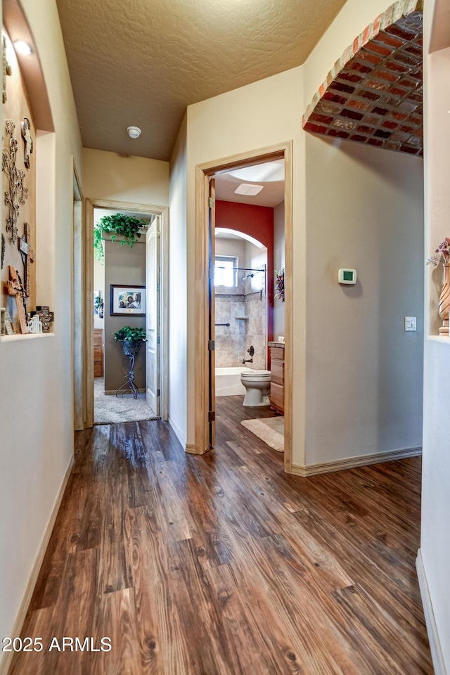 corridor with a textured ceiling, baseboards, and wood finished floors