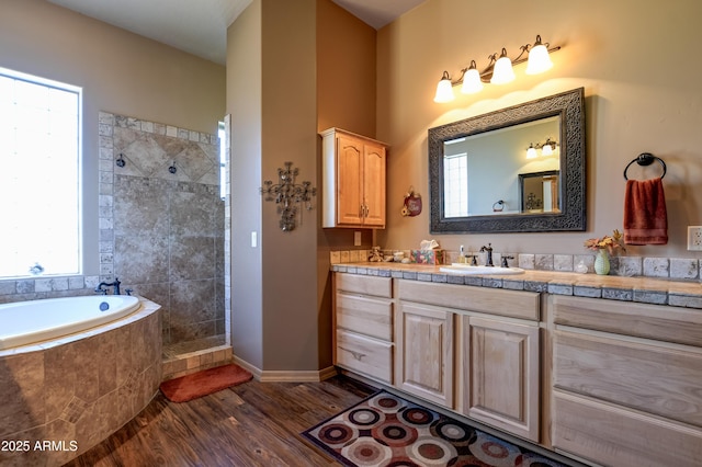 bathroom with a walk in shower, vanity, a garden tub, wood finished floors, and baseboards