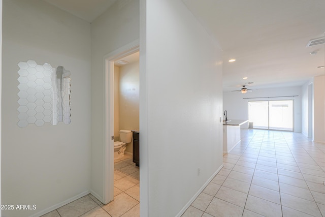 corridor with light tile patterned floors, a sink, visible vents, and baseboards