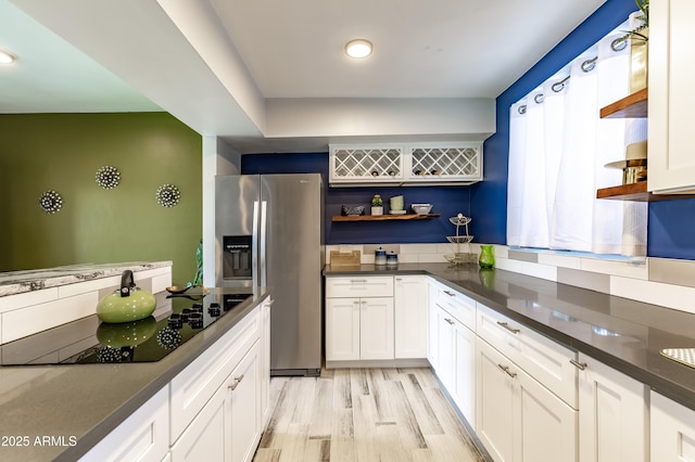 kitchen with black electric stovetop, white cabinets, stainless steel fridge with ice dispenser, and light hardwood / wood-style flooring