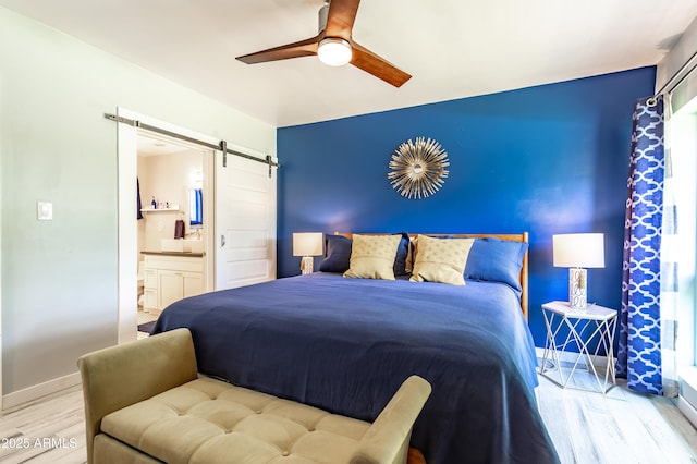 bedroom featuring ceiling fan, connected bathroom, a barn door, and light wood-type flooring