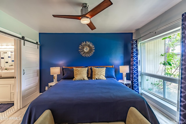 bedroom with ceiling fan, multiple windows, ensuite bathroom, and a barn door