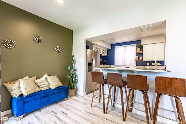 kitchen with kitchen peninsula, white cabinetry, light wood-type flooring, a breakfast bar area, and stainless steel fridge