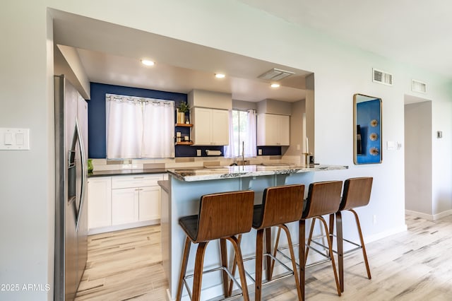 kitchen with white cabinets, a kitchen bar, dark stone counters, stainless steel fridge, and light hardwood / wood-style flooring