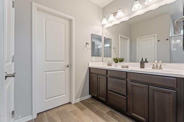 full bath featuring double vanity, a sink, baseboards, and wood finished floors