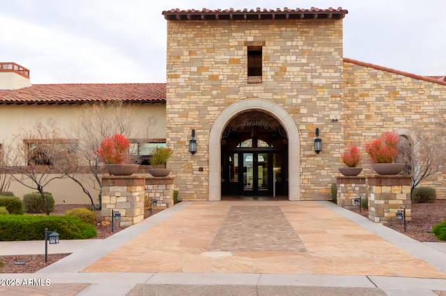 view of exterior entry featuring stucco siding, a tiled roof, stone siding, and french doors