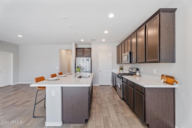 kitchen featuring a center island with sink, sink, appliances with stainless steel finishes, light hardwood / wood-style floors, and a breakfast bar area