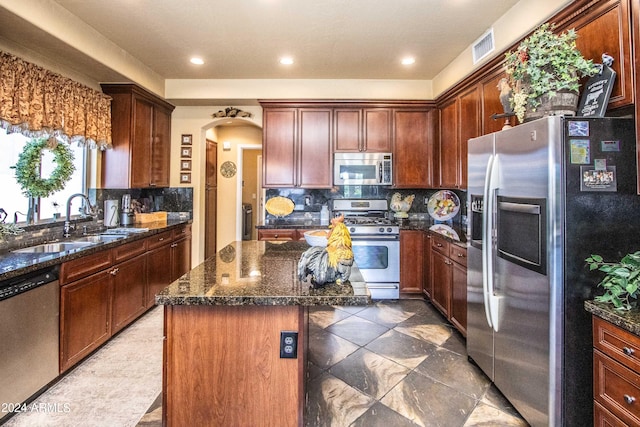 kitchen with tasteful backsplash, dark stone counters, stainless steel appliances, sink, and a center island