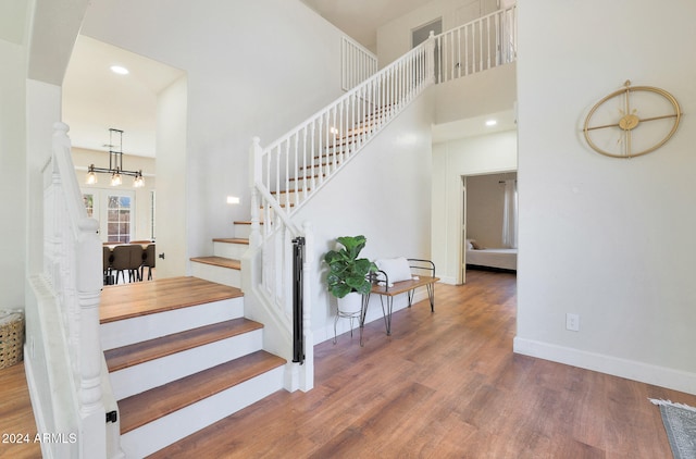 staircase with a towering ceiling, a notable chandelier, and wood-type flooring