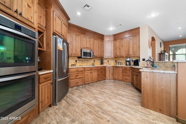 kitchen featuring sink, stainless steel appliances, light stone counters, tasteful backsplash, and light wood-type flooring