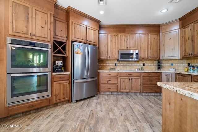 kitchen with light stone counters, appliances with stainless steel finishes, light hardwood / wood-style floors, and decorative backsplash