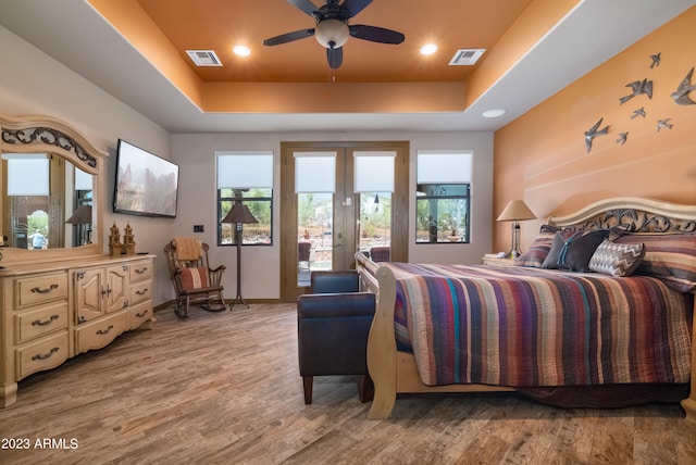 bedroom featuring ceiling fan, a tray ceiling, access to exterior, and light hardwood / wood-style flooring