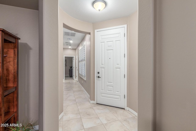 corridor featuring visible vents, baseboards, and light tile patterned flooring