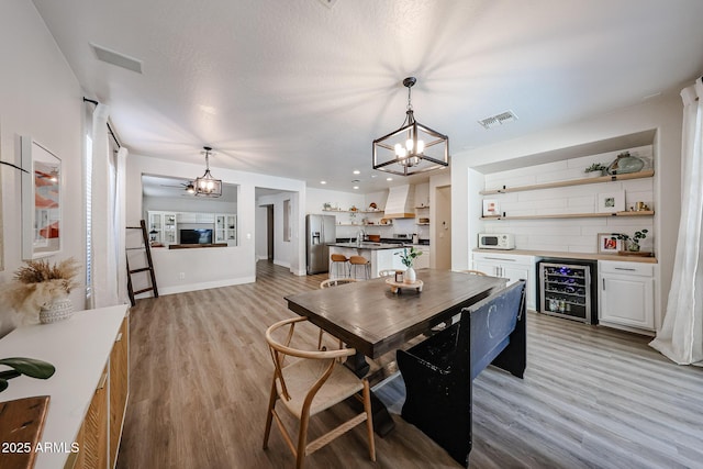 dining space featuring a notable chandelier, sink, beverage cooler, and light hardwood / wood-style floors