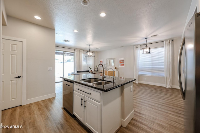 kitchen with decorative light fixtures, white cabinetry, sink, stainless steel appliances, and a center island with sink