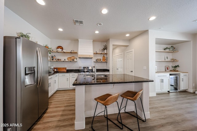 kitchen with sink, appliances with stainless steel finishes, white cabinetry, a kitchen island with sink, and wine cooler