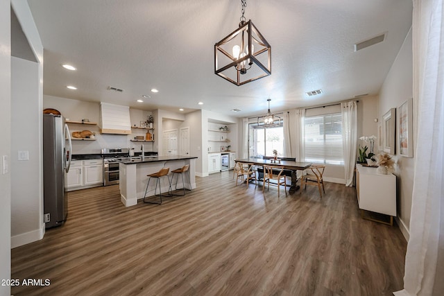 kitchen featuring pendant lighting, stainless steel fridge, wood-type flooring, white cabinets, and a kitchen bar