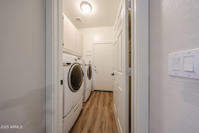 washroom with cabinets, a textured ceiling, independent washer and dryer, and light hardwood / wood-style floors