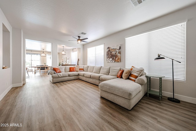 living room featuring wood-type flooring, ceiling fan with notable chandelier, and a textured ceiling