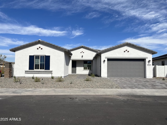 mediterranean / spanish home featuring a garage, decorative driveway, a tiled roof, and stucco siding