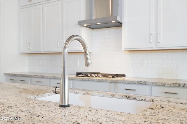 details featuring light stone countertops, tasteful backsplash, wall chimney exhaust hood, and white cabinetry