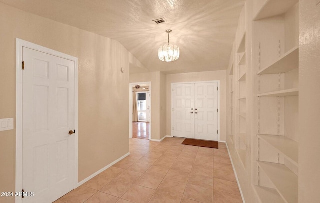 foyer entrance with lofted ceiling, light tile patterned floors, a textured ceiling, and an inviting chandelier