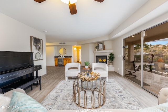 living area with visible vents, baseboards, light wood-style floors, a glass covered fireplace, and a ceiling fan