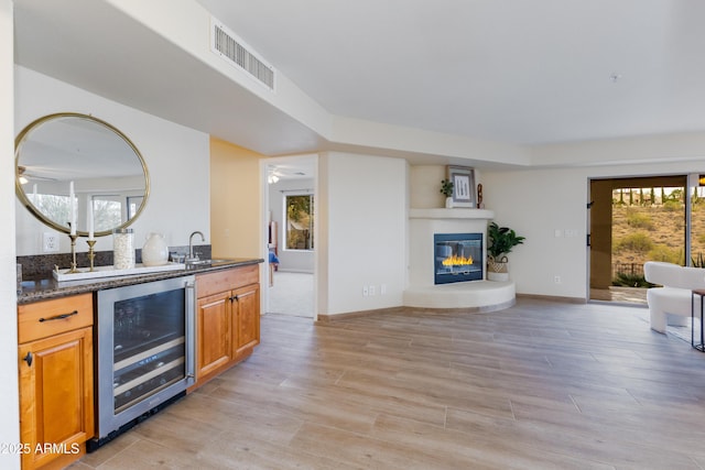 kitchen with dark stone countertops, beverage cooler, visible vents, a glass covered fireplace, and open floor plan