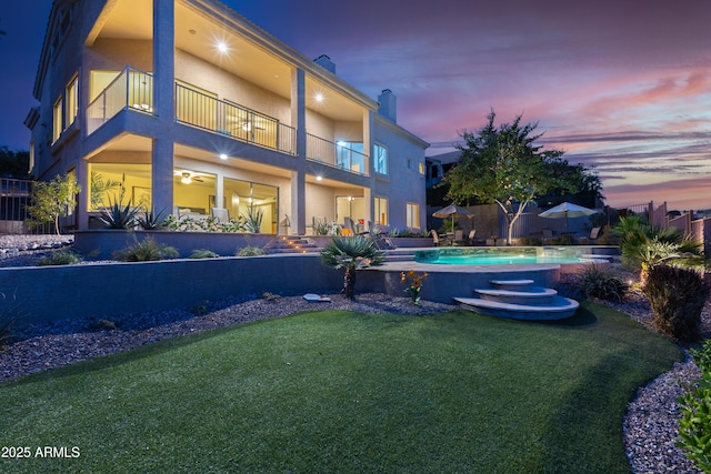 rear view of property with stucco siding, a balcony, a lawn, and a chimney