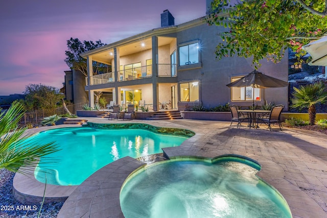 pool at dusk featuring outdoor dining area, a patio, a pool with connected hot tub, and fence