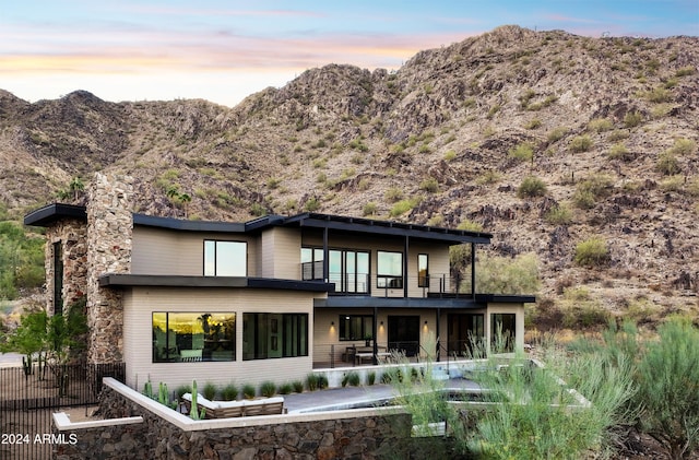 back house at dusk featuring a balcony, a mountain view, and a patio