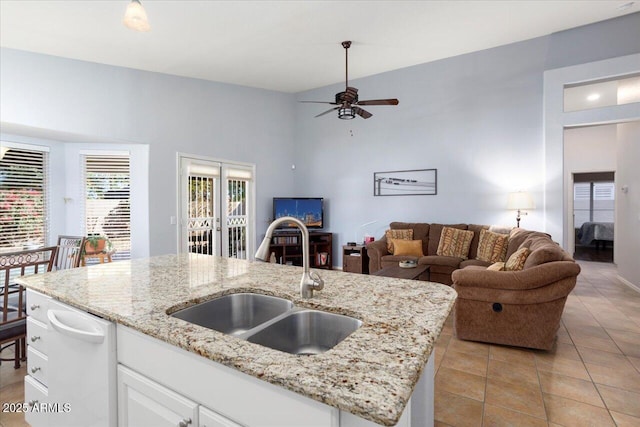 kitchen featuring a kitchen island with sink, sink, ceiling fan, light stone counters, and white cabinetry