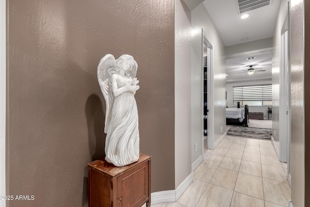 hallway featuring visible vents, a textured wall, baseboards, and light tile patterned floors
